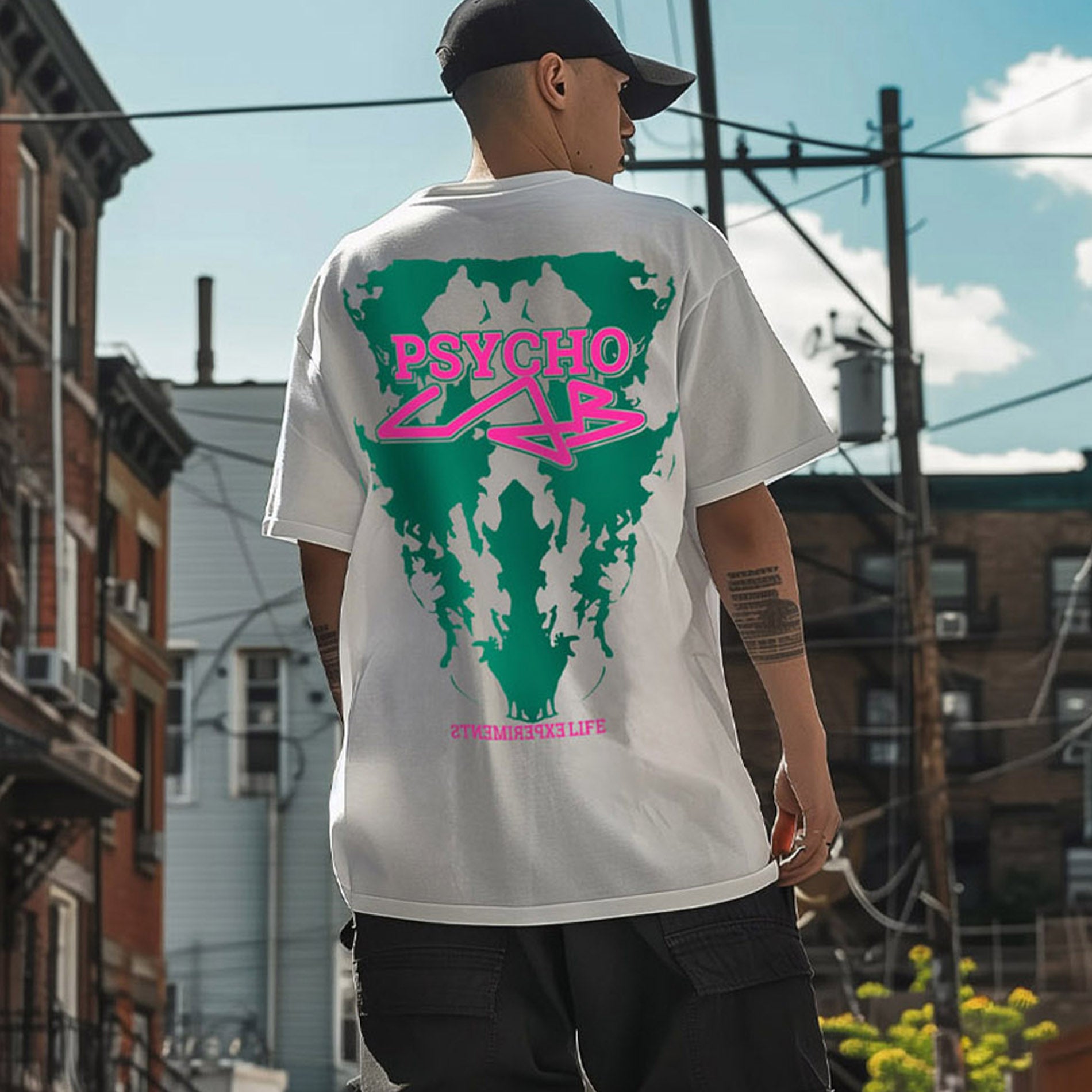 T-Shirt Emotion von PsychoLab, präsentiert auf einem urbanen Hintergrund mit auffälligem, grünem und pinkem Grafikdesign auf dem Rücken, ideal für stilbewusste Streetwear-Liebhaber, die den PsychoLab-Look verkörpern.